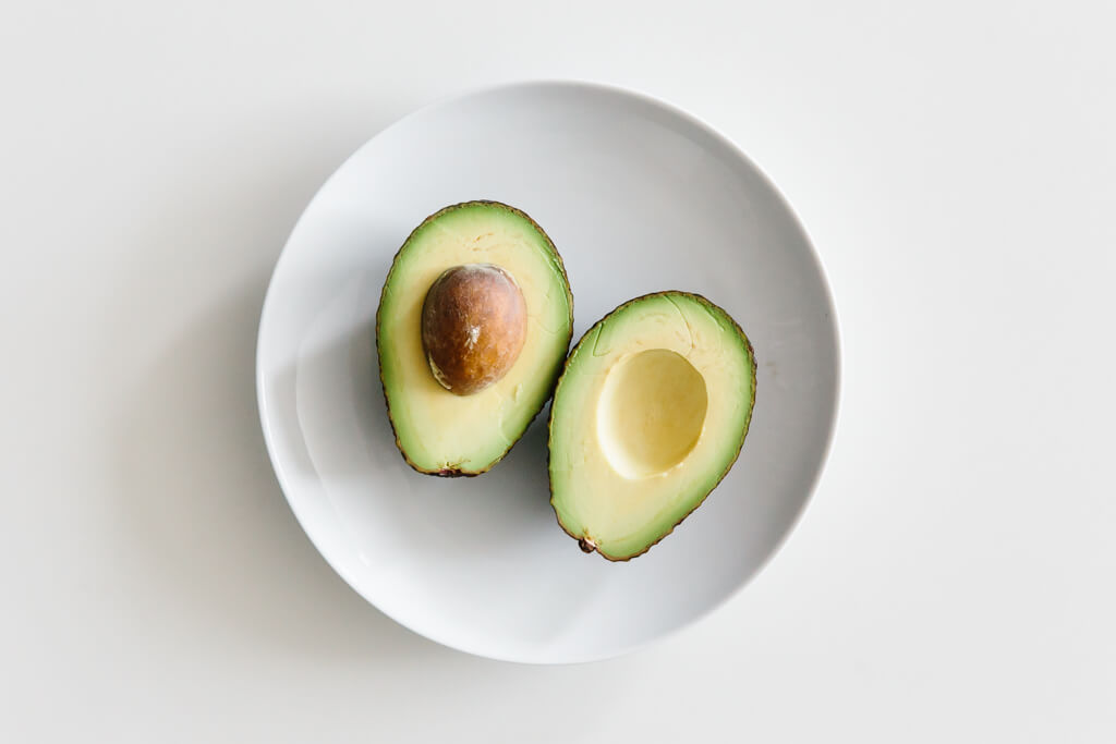 Plate of avocado sliced in half on a white table.