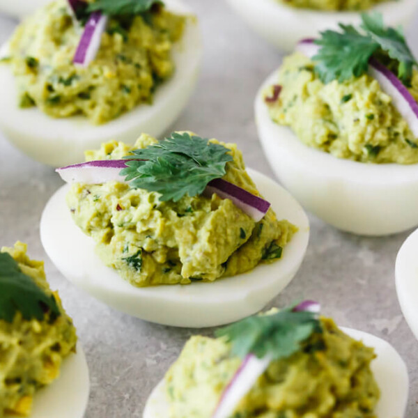 Several avocado guacamole deviled eggs on a white plate.