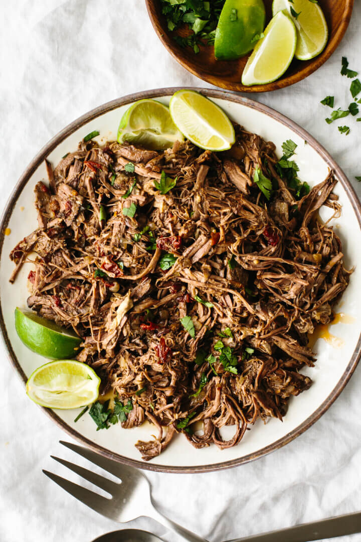 Beef barbacoa on a plate with lime wedges.