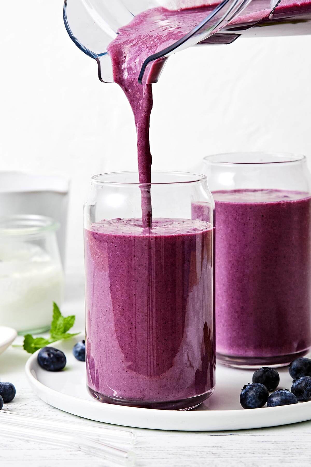 Pouring blueberry smoothie into a cup.