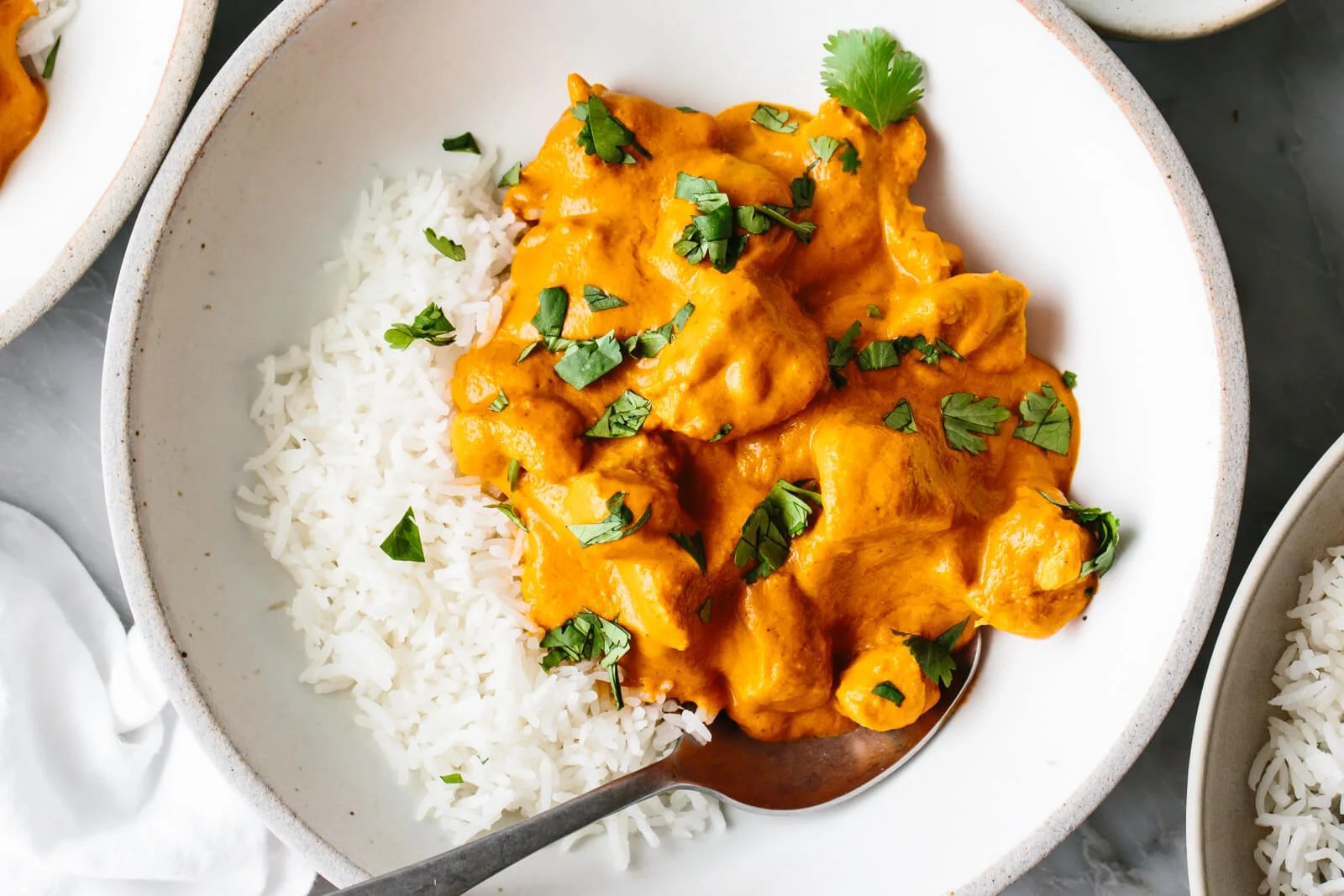 A bowl with butter chicken and rice with a spoon