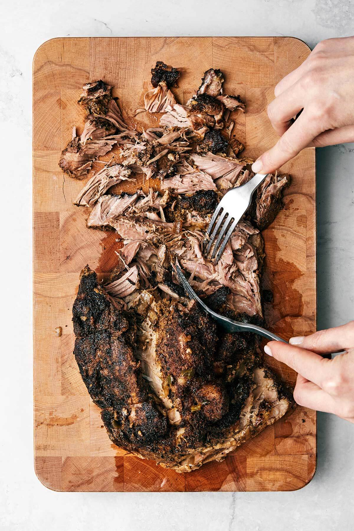 Shredding carnitas on a wooden board.