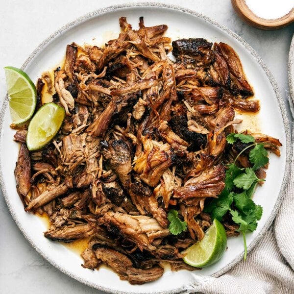 Carnitas on a plate next to tortillas.