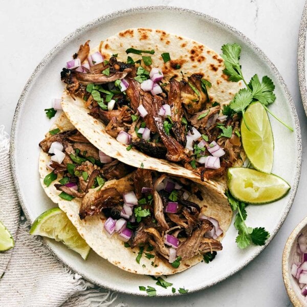 A plate of carnitas tacos with limes.