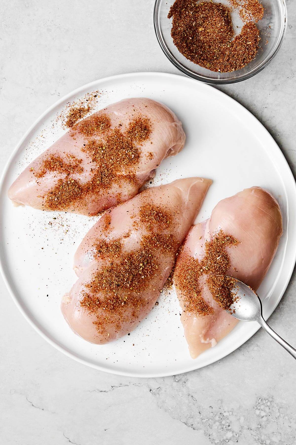 Adding fajita seasoning on chicken breasts.