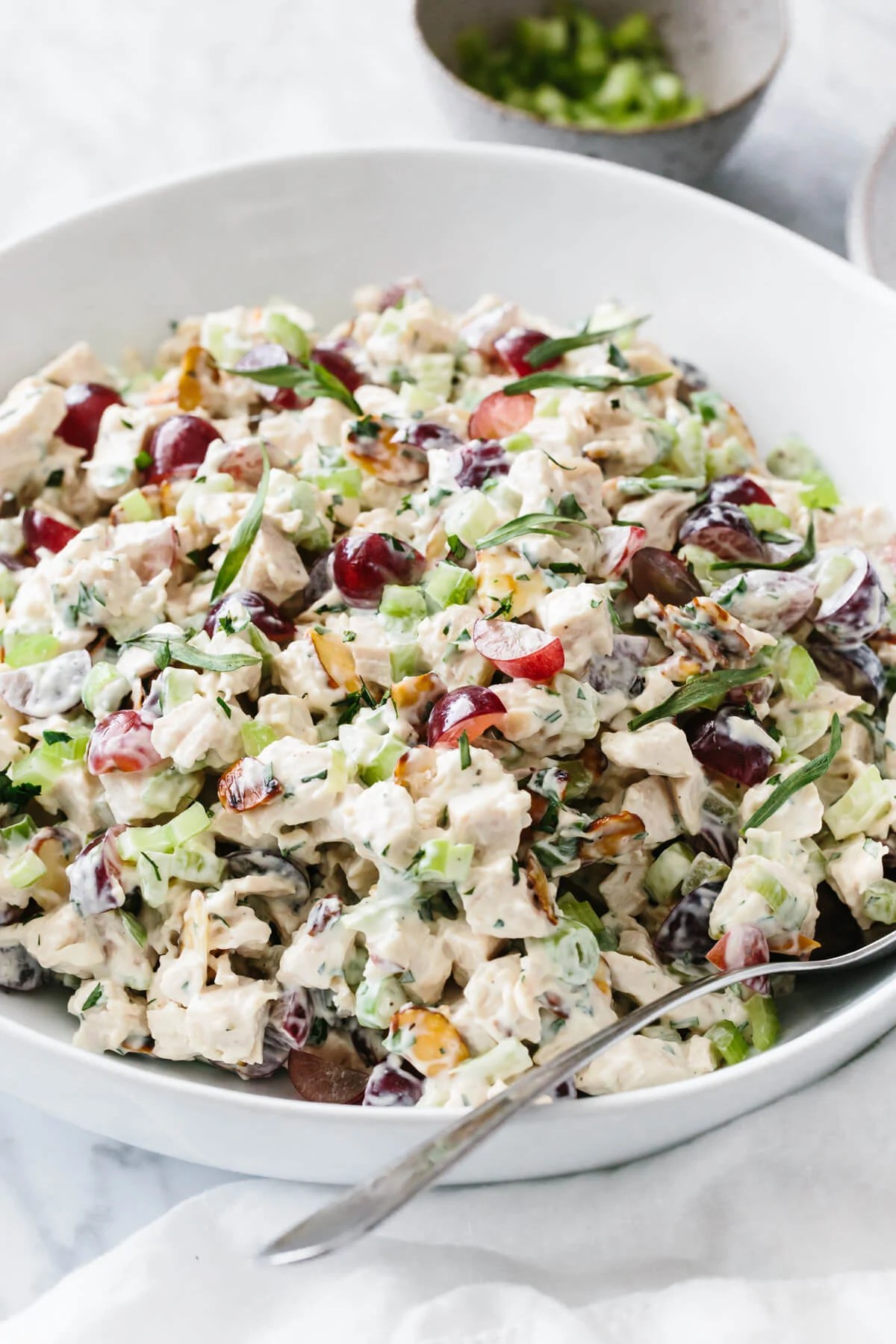 Chicken salad in a white bowl with spoon and small bowl of diced celery in the background.