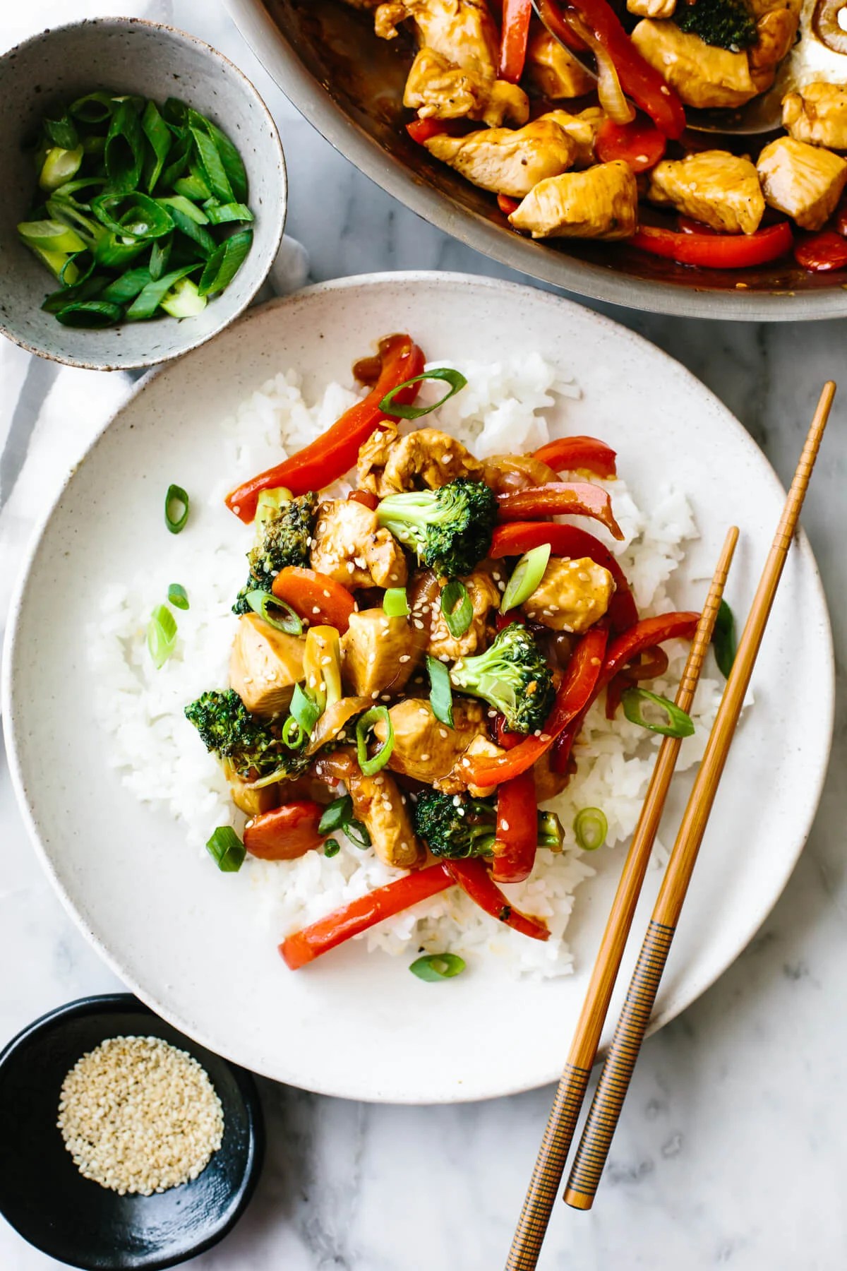 Chicken stir-fry on a plate with rice next to green onions.