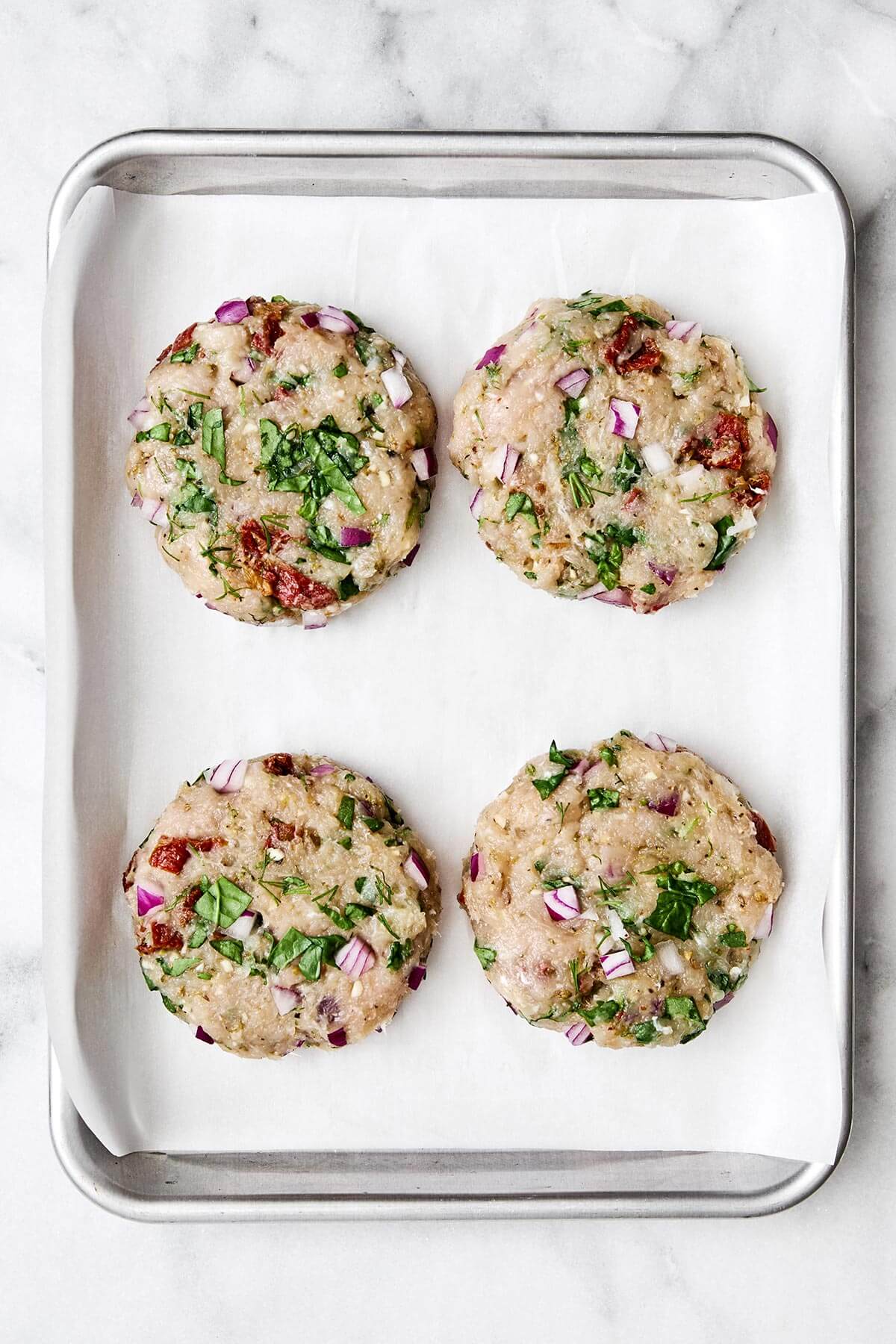 Greek chicken burger patties on a sheet pan.