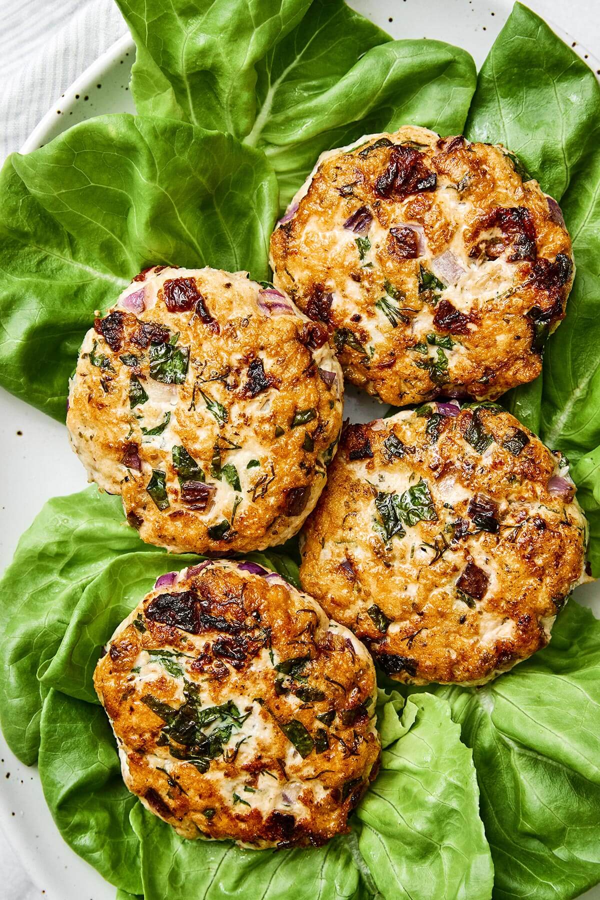 Greek chicken burgers on a plate with lettuce.