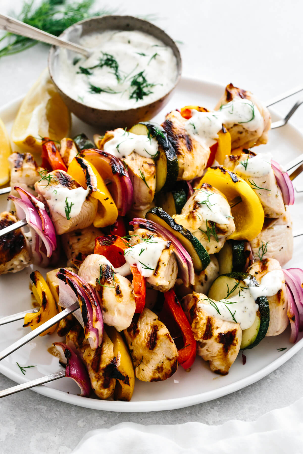 Skewers of greek chicken kabobs with a bowl of tzaztiki.