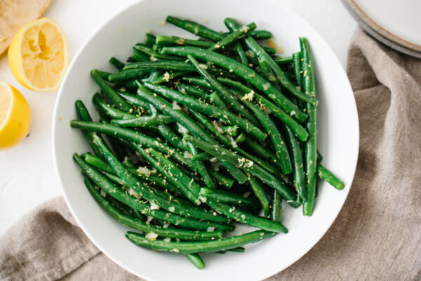 Green beans topped with lemon in a white bowl.