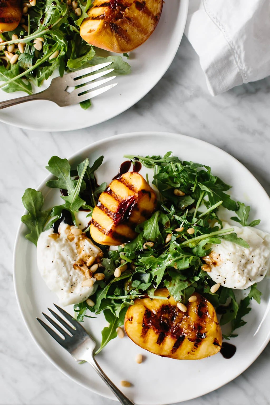 This grilled peach and burrata salad is summertime on a plate. The mix of grilled peaches, arugula, burrata, pine nuts and balsamic is the perfect summer salad recipe.