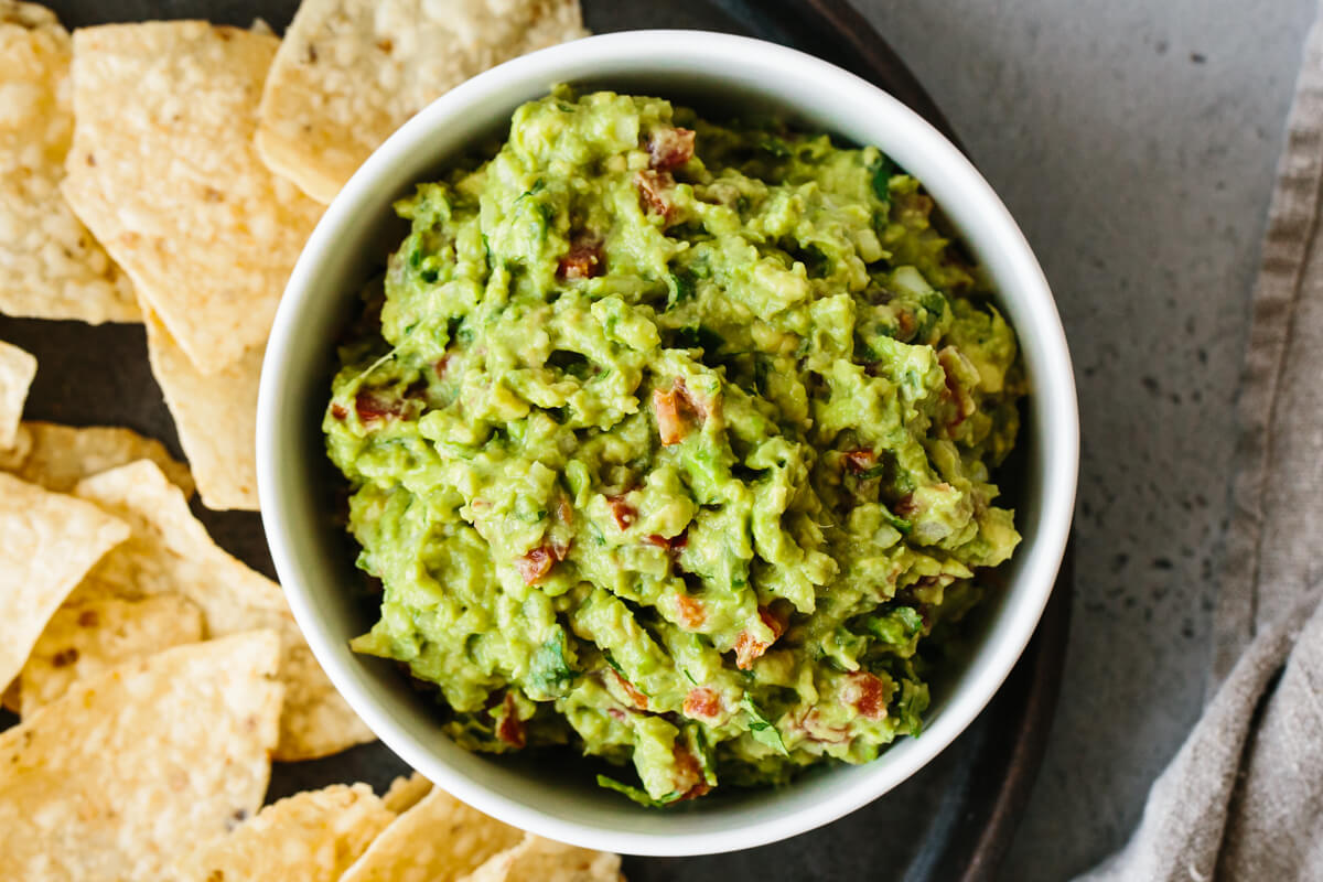 Guacamole recipe in a bowl next to tortilla chips.