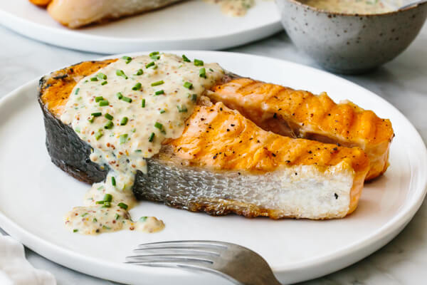 Salmon steak on a plate drizzled with yogurt sauce.