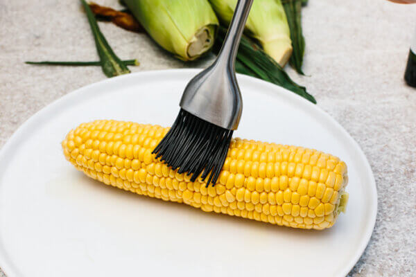 Brushing oil on a corn on the cob for grilling