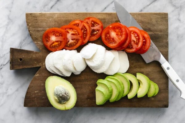 A wooden board with sliced avocado caprese ingredients