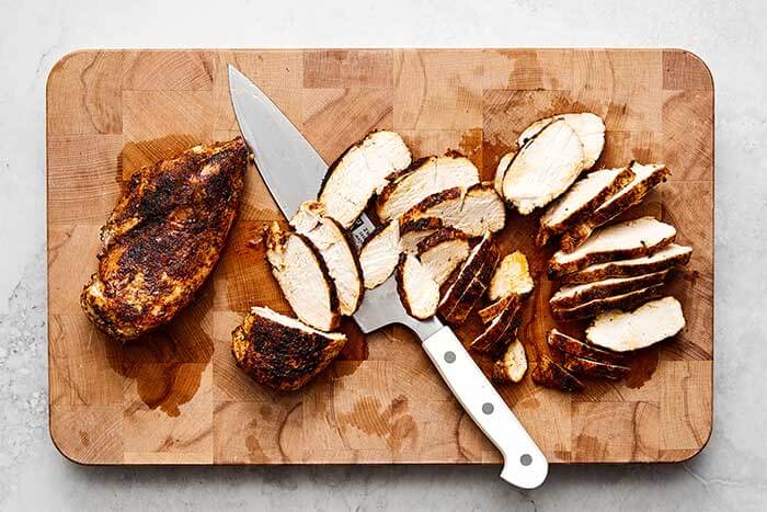 Sliced chicken breasts on a wooden chopping board.