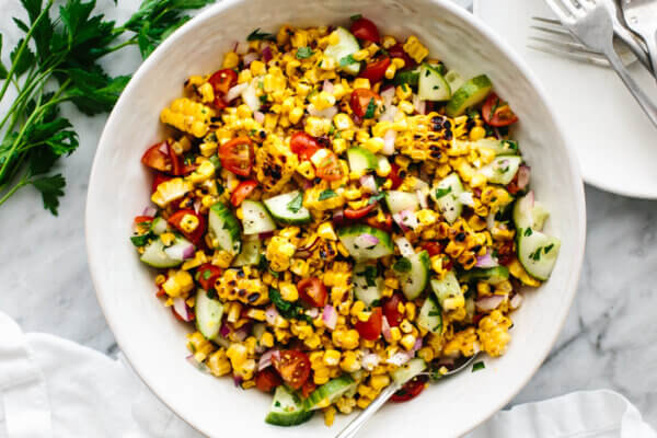 A white bowl of corn salad next to a fork.