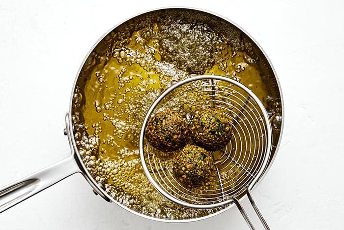 Adding falafel to a pot of oil.