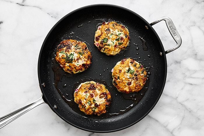 Greek chicken burger patties in a pan.