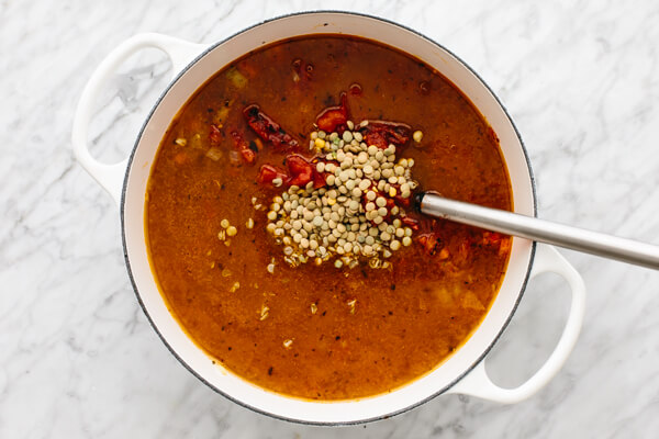 Adding lentils into a pot of lentil soup.