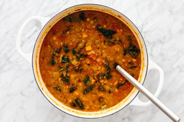 A big white pot with lentil soup on a table with a serving spoon.