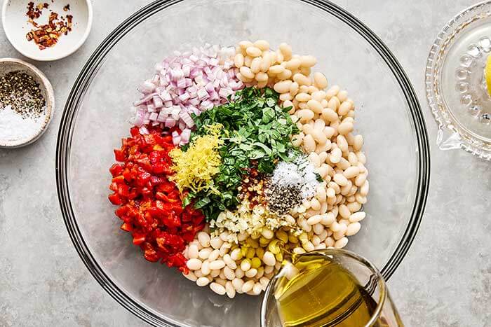 Mixing marinated white. beans in a bowl.