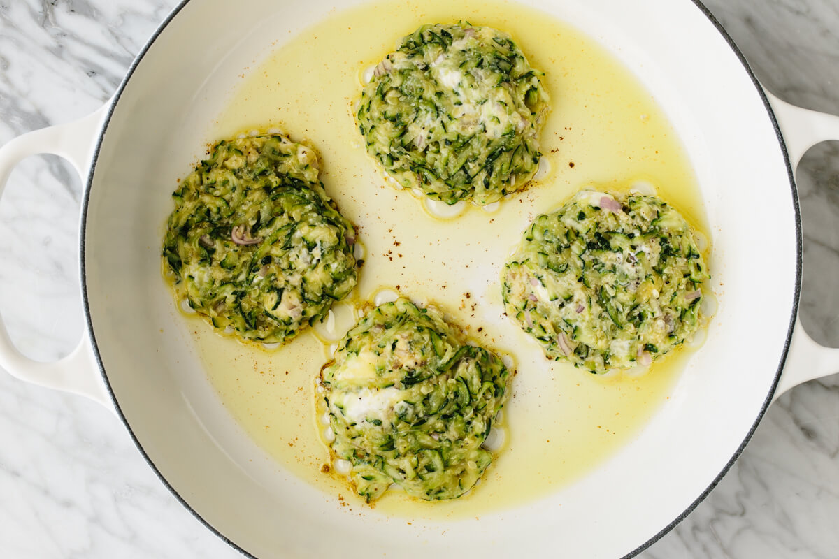 Zucchini fritters frying in a pan with oil.