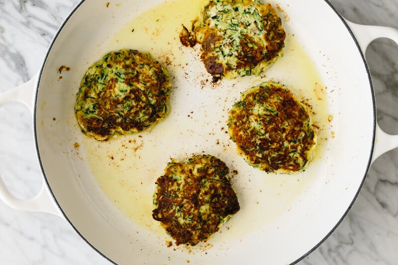 Zucchini fritters in a pan golden on one side.