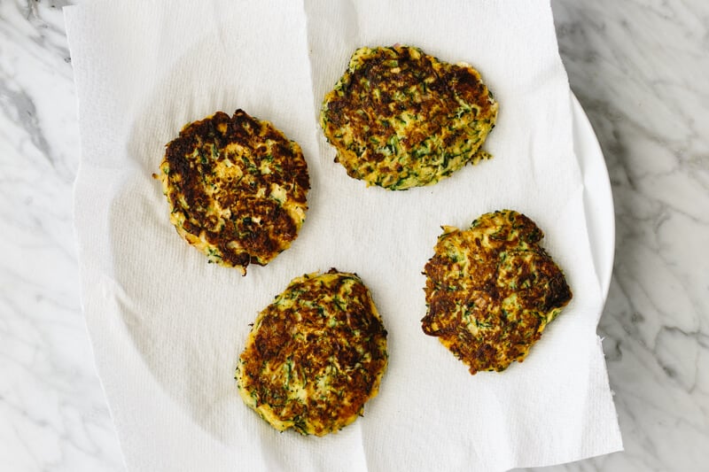 Zucchini fritters on a paper towel lined plate.