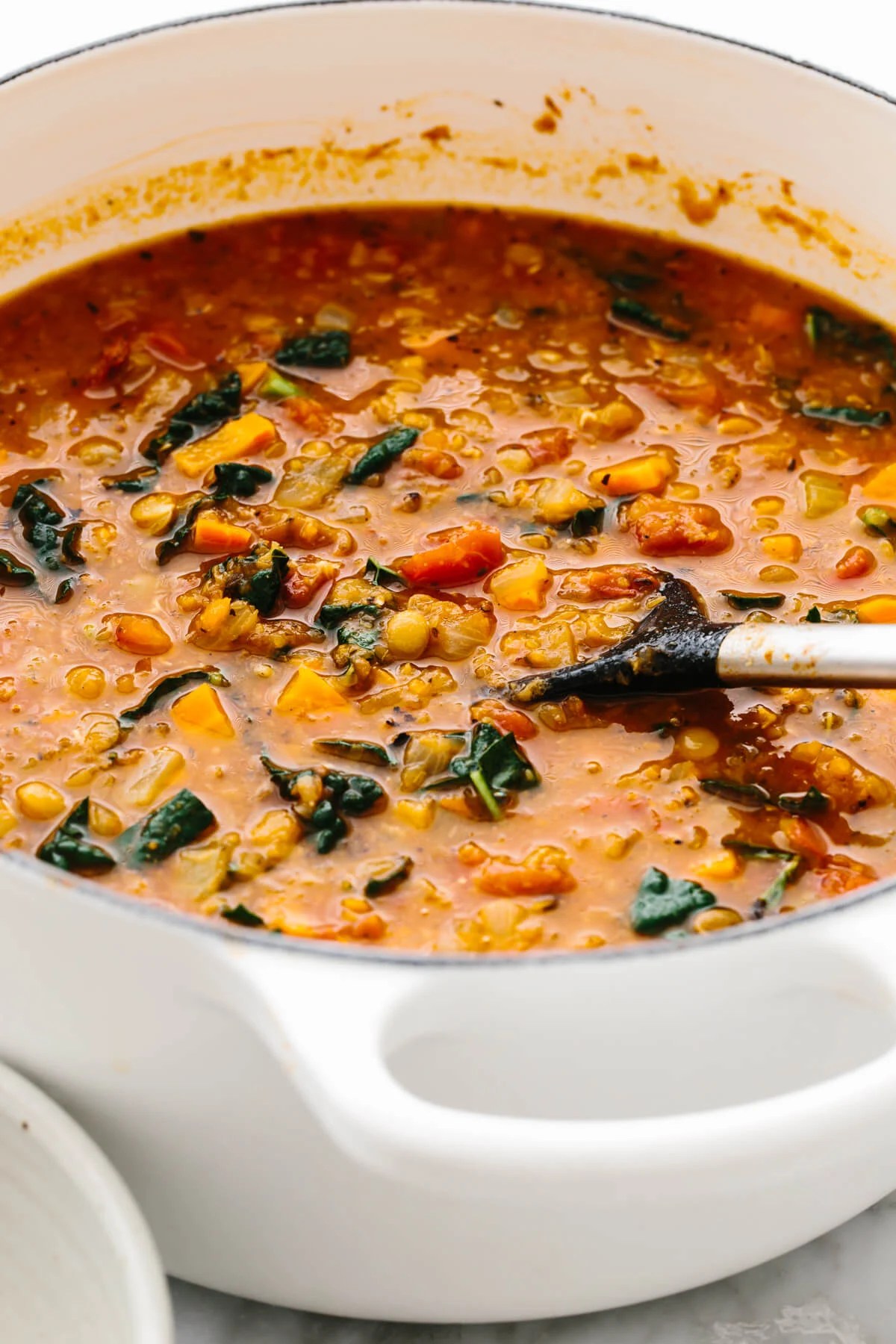 A white pot with lentil soup and a spoon in it.