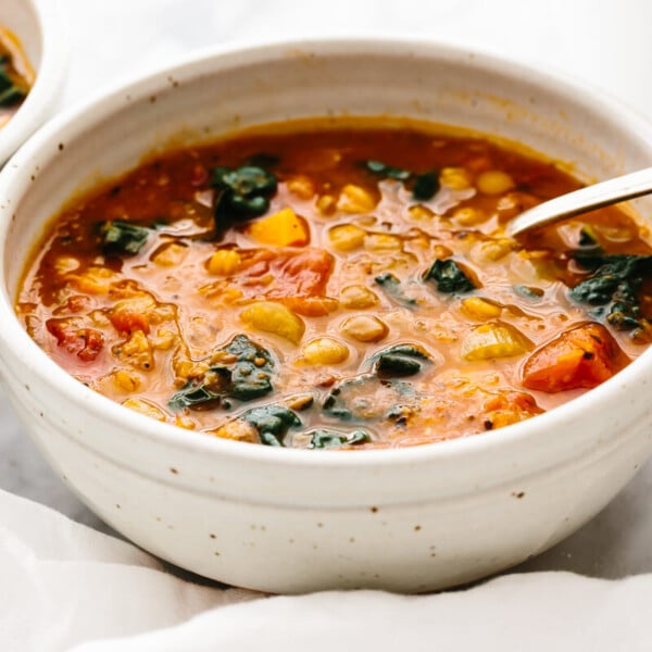 A white bowl with lentil soup and a spoon on a table.