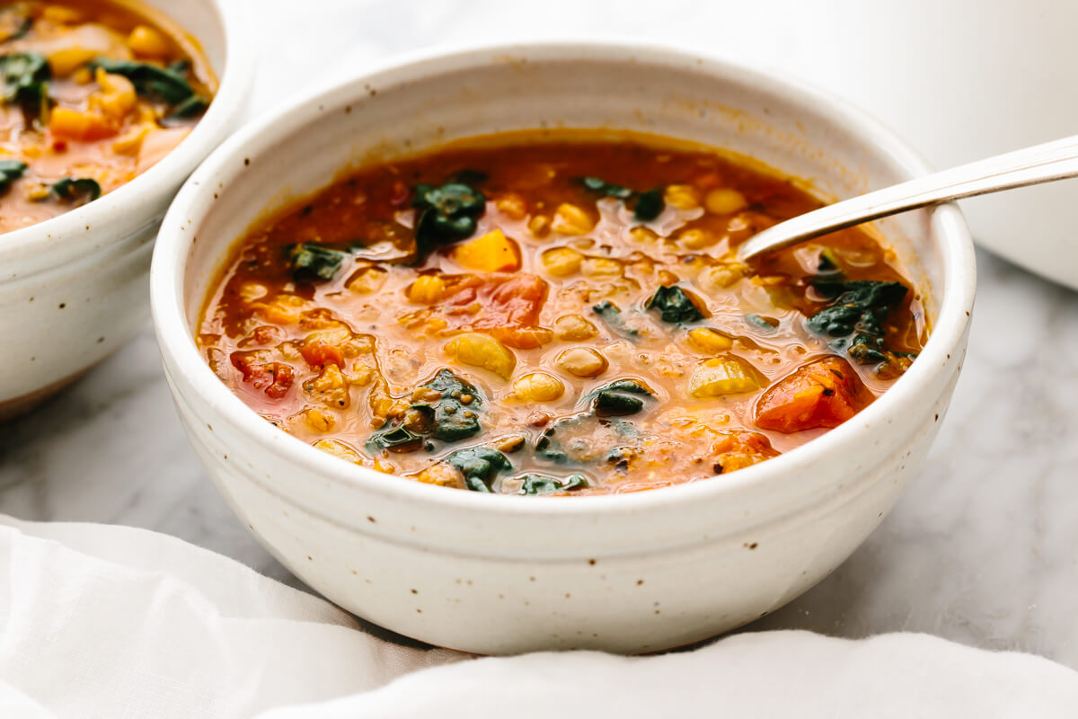 A white bowl with lentil soup and a spoon on a table.