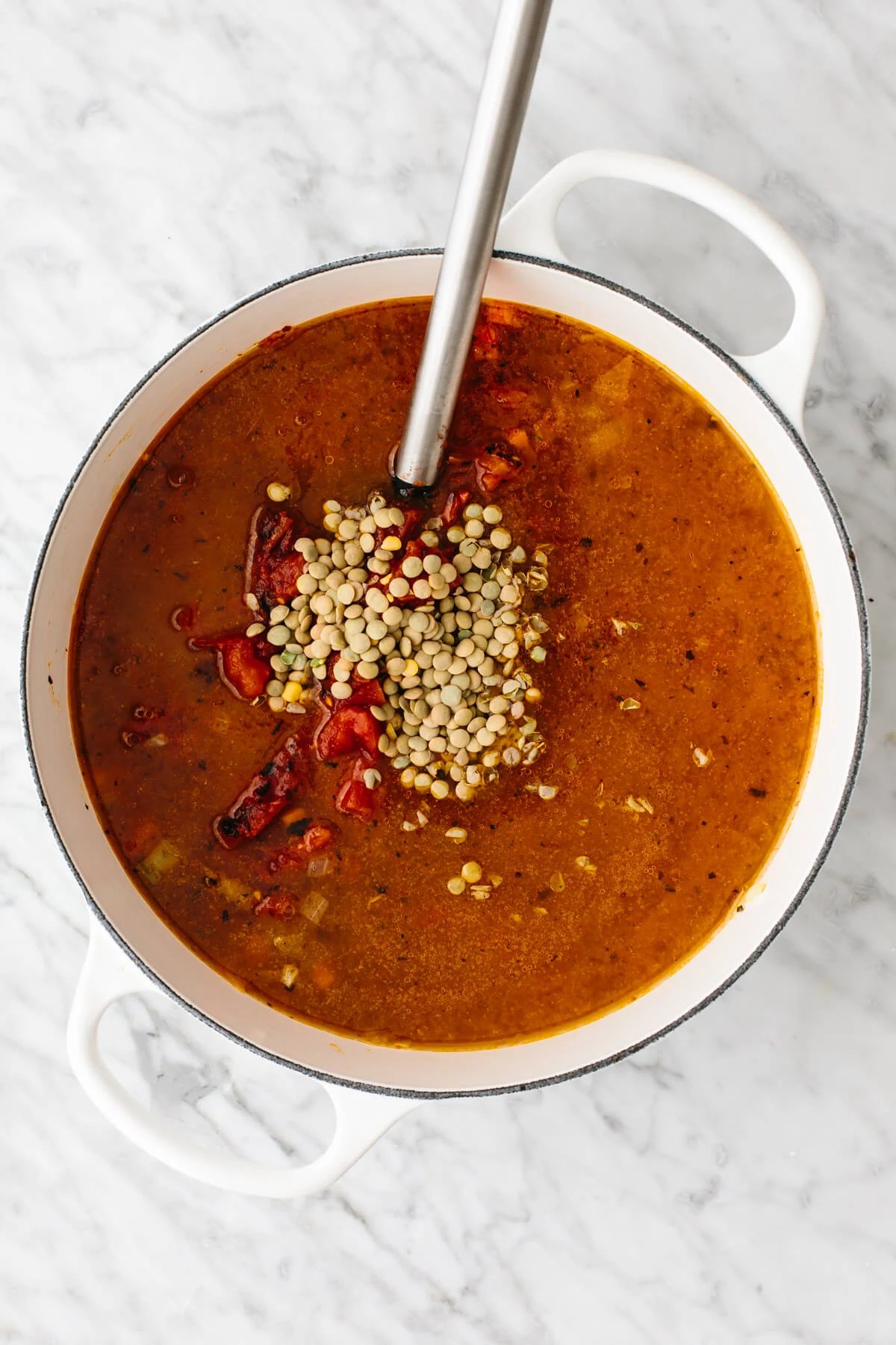 Adding in broth into a pot of lentil soup