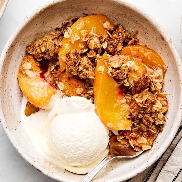 A bowl of peach crisp with ice cream.