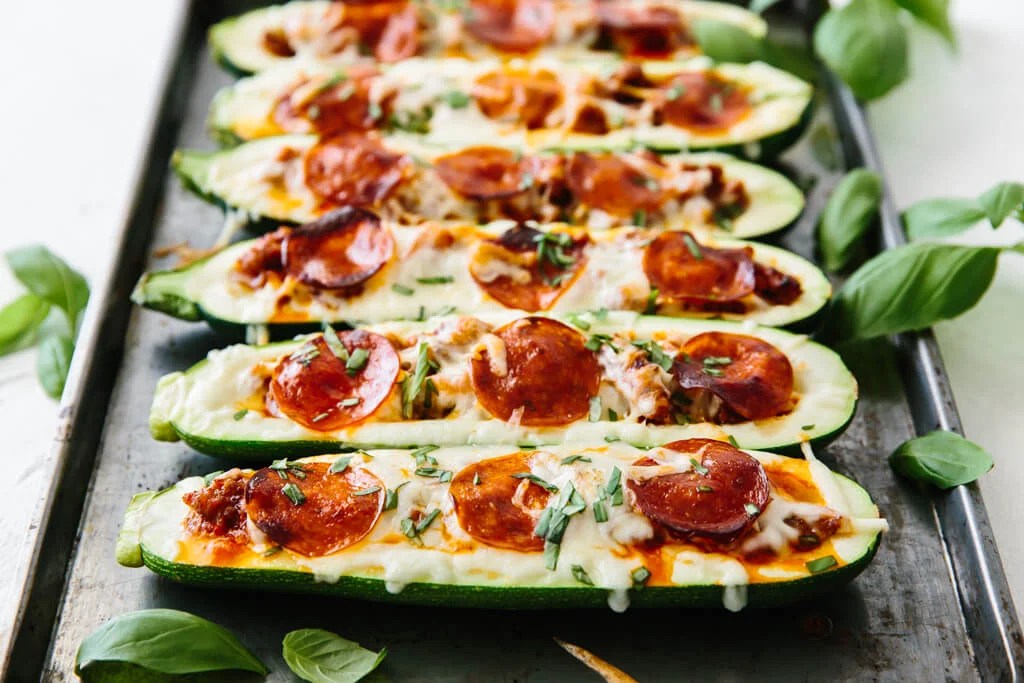 Stuffed zucchini with pizza toppings on a baking tray.