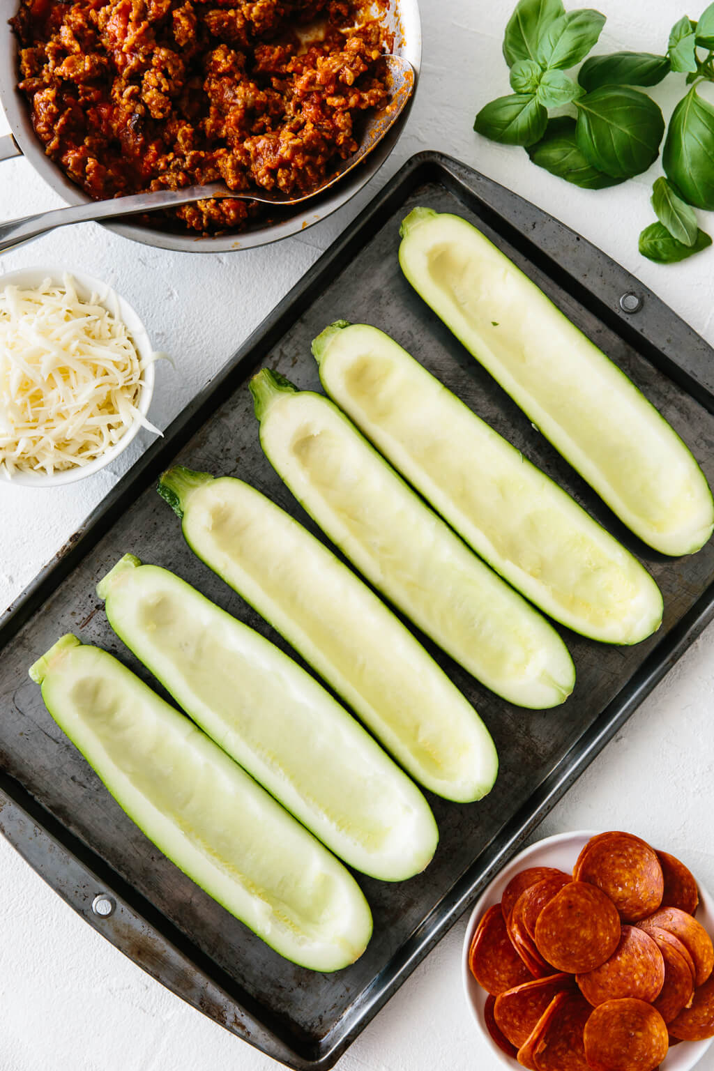 Zucchini sliced in half with seeds scooped out on a baking tray.