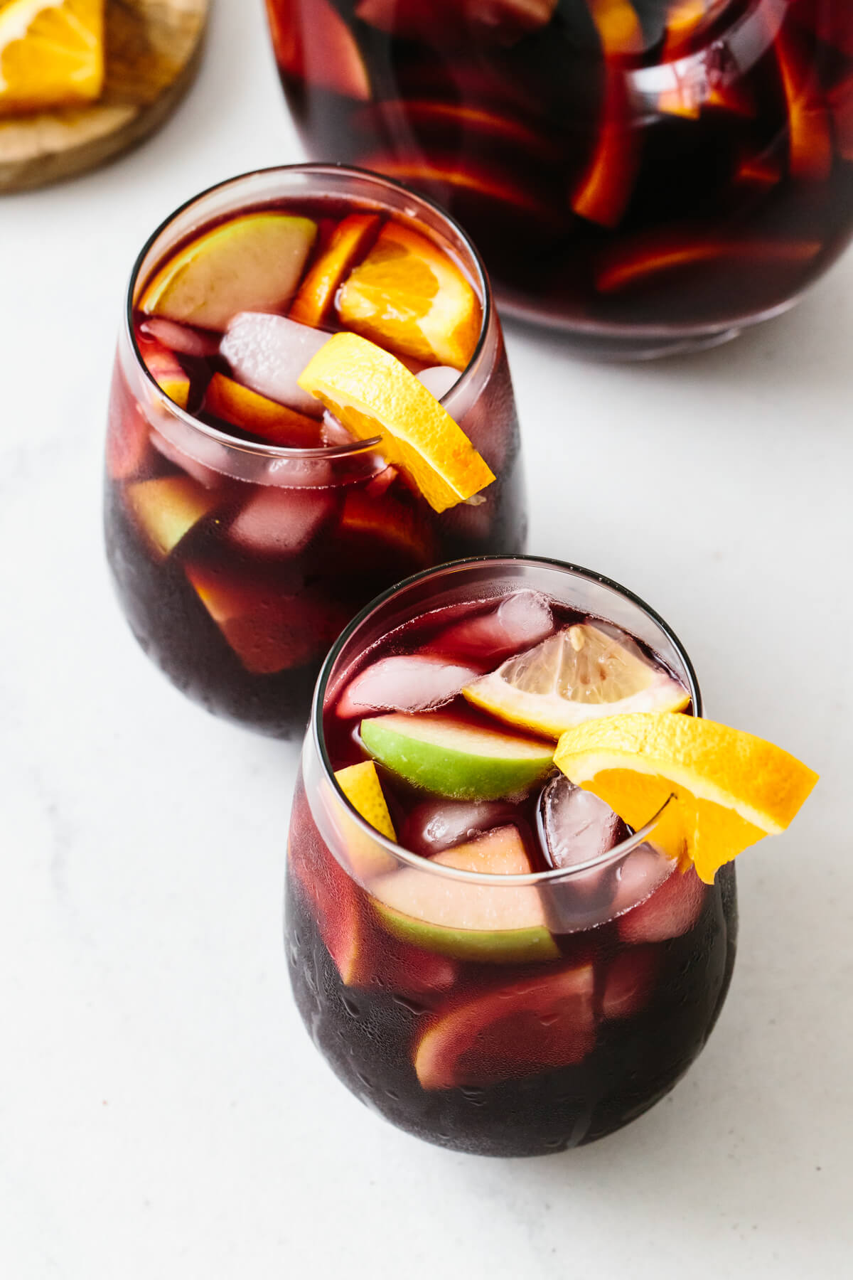 Two glasses of red sangria with orange garnishes.