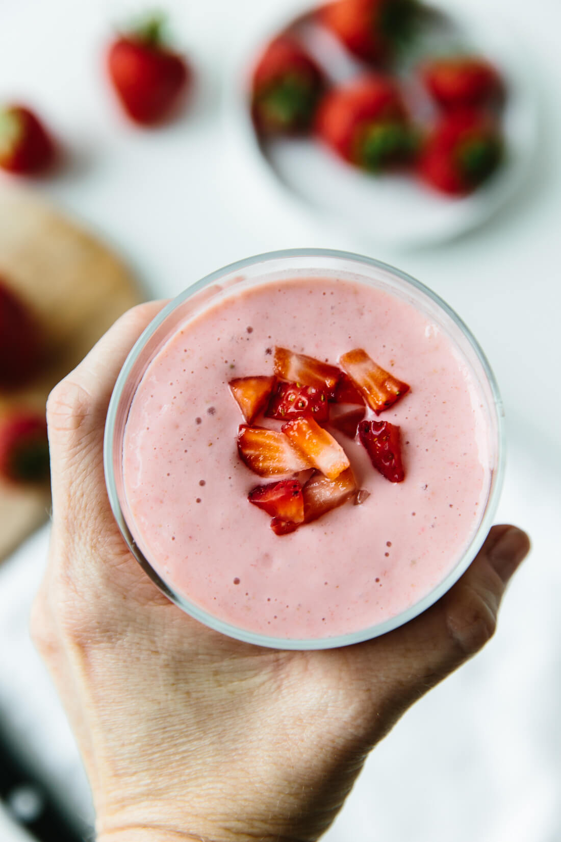 Hand holding glass of strawberry banana smoothie. 