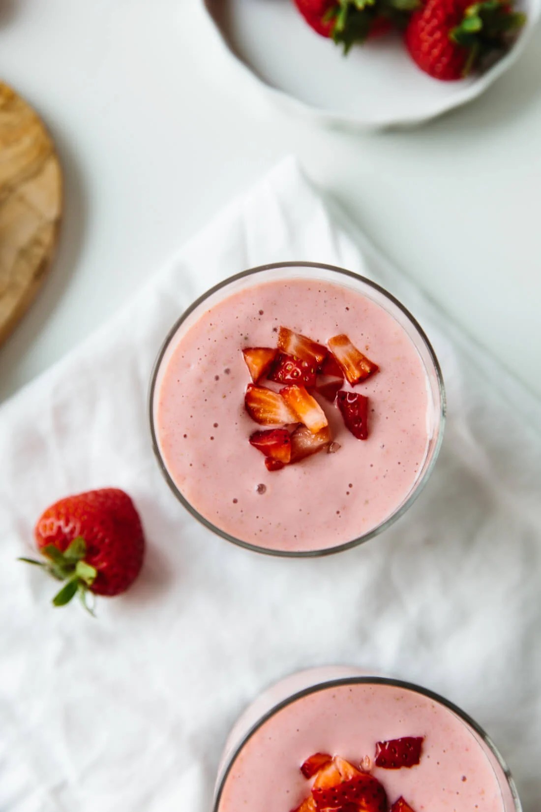 Strawberry banana smoothie recipe in two glasses with fresh strawberries beside it.