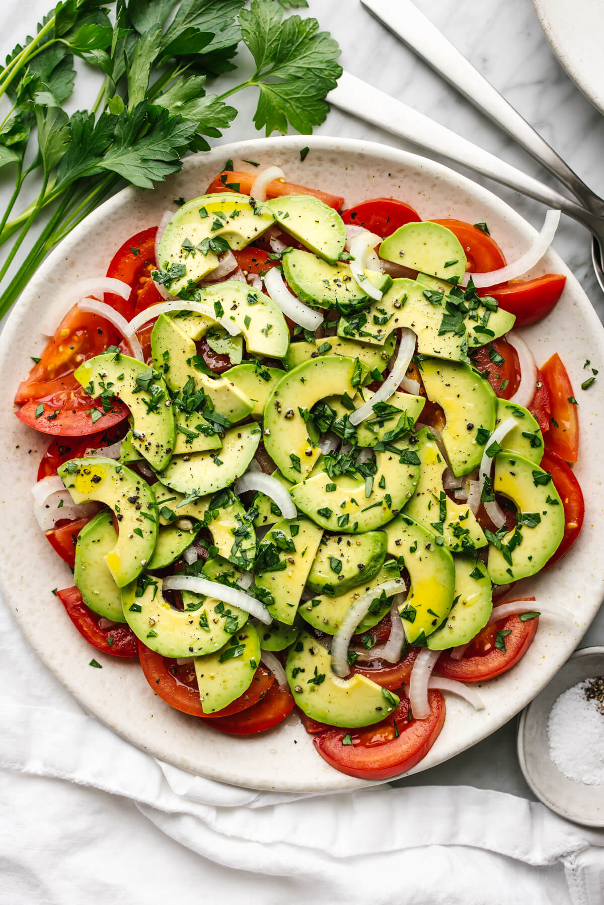 Tomato, onion, avocado salad on a plate next to parsley.