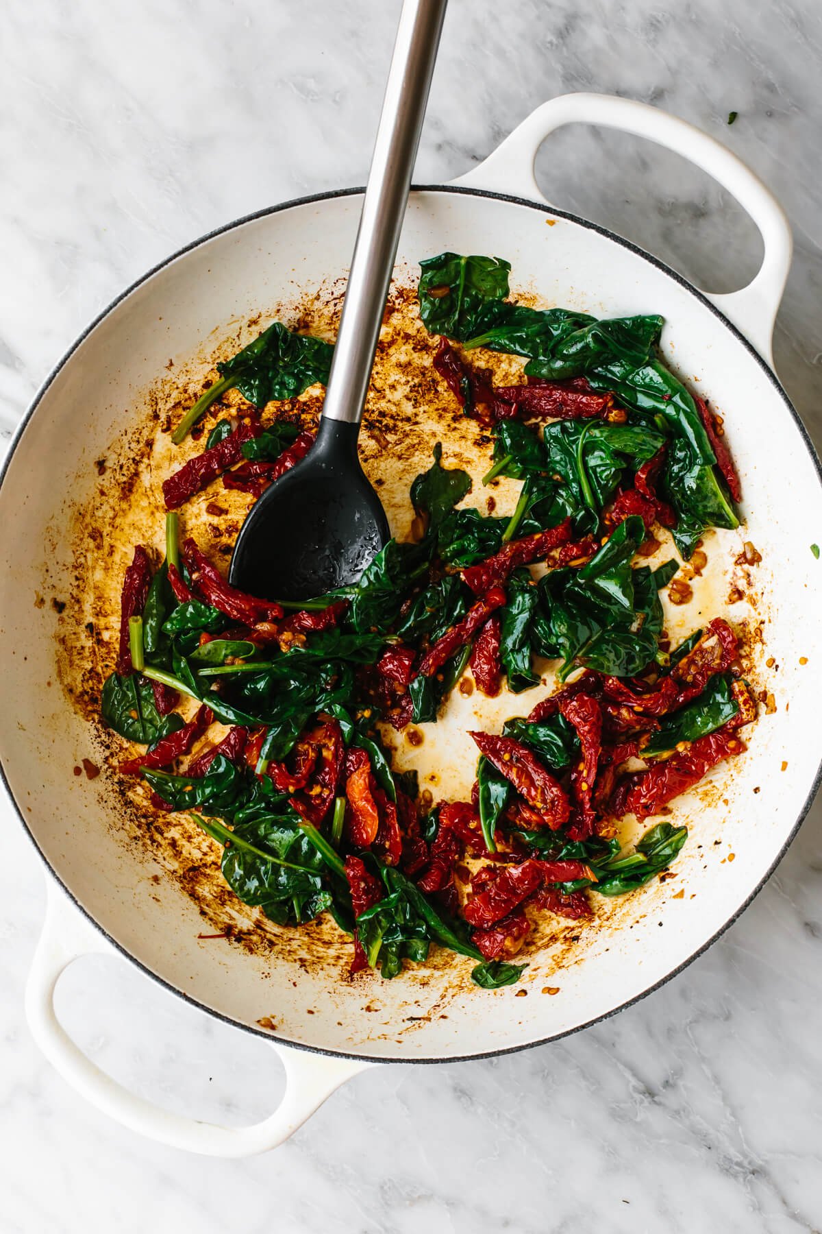 Cooking spinach and tomatoes in a skillet for tuscan chicken